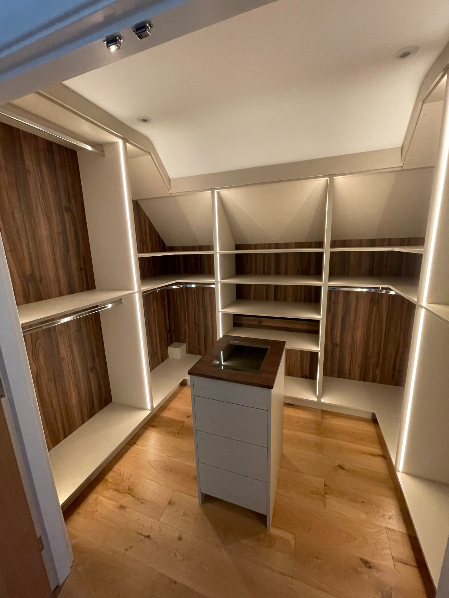 Walk-in wardrobe interior with warm wood panelling, integrated LED lighting and central island drawers, handcrafted by Webb Bespoke Interiors